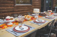 a long table with plates and desserts on it in front of a wooden cabin