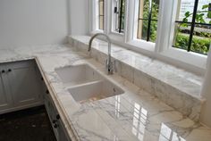 a kitchen with marble counter tops and white cabinets in the corner, along with two windows