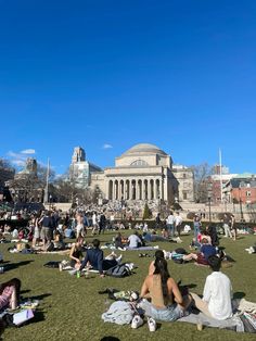 many people are sitting on the grass in front of a building