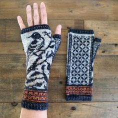 a woman's hand with two knitted mitts on top of a wooden table