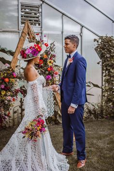 a man and woman standing next to each other in front of a greenhouse filled with flowers