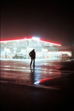 a man standing in front of a gas station at night with his back to the camera