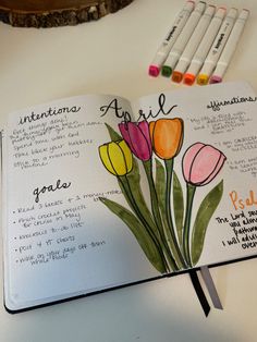 an open notebook with markers and some flowers