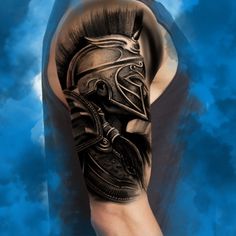 a man's arm with a black and grey tattoo on it, featuring a spartan helmet