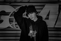 a young man in a black hoodie and hat standing next to a wall with letters on it