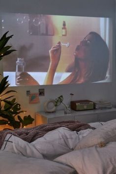 a woman laying in bed while watching a movie on the wall behind her is a potted plant