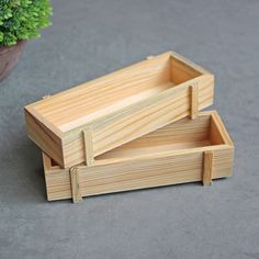 two wooden trays sitting next to each other on top of a cement floor near a potted plant