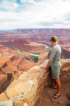 a man standing at the edge of a cliff looking out over a river and canyon