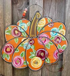 an orange pumpkin hanging on a wooden fence with flowers painted on the front and sides