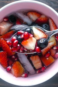 a bowl filled with fruit and ice cream on top of a wooden table next to a spoon