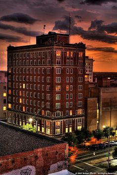 the sun is setting over an old building and cars are parked on the street in front of it