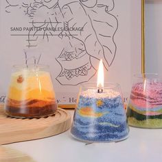 three candles sitting on top of a table next to a drawing and painting frame in the background