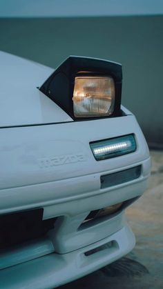 the front end of a white sports car with its lights on and headlamps down