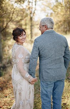 an older man and woman holding hands in the woods