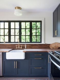 a kitchen with dark blue cabinets and white counter tops is pictured in this image, there are windows that look out onto the trees outside