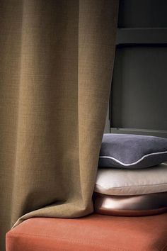 pillows are stacked on top of an orange ottoman in front of a window with curtains