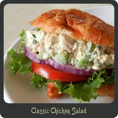 a chicken salad sandwich with lettuce, tomato and onion on a croissant roll