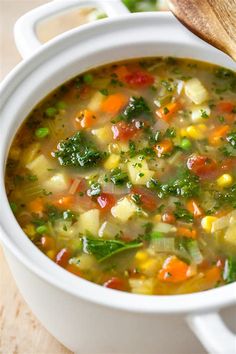 a white bowl filled with vegetable soup on top of a wooden cutting board next to a spoon