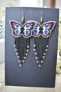 a pair of beaded earrings on top of a black card next to a potted plant