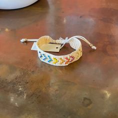 a white bracelet with multicolored beads and a tag on the end is sitting on a table