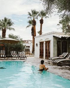 a woman is sitting in the middle of a swimming pool surrounded by lounge chairs and palm trees