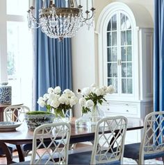 a dining room table with white flowers in vases on it and blue drapes