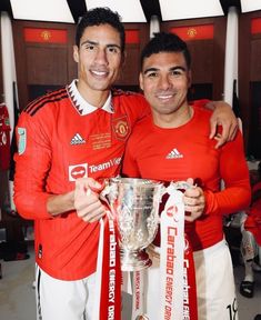 two men standing next to each other holding a soccer trophy and posing for the camera