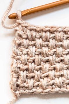 the crochet stitch is being worked on with a wooden knitting needle in front of it