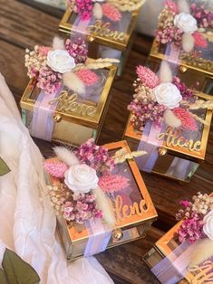 four small boxes with flowers on them sitting on top of a wooden table next to white and pink ribbons