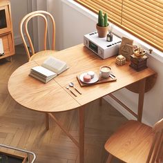 a wooden table with two chairs and an open book on it next to a window