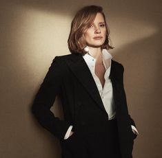 a woman in a black suit and white shirt is posing for a photo with her hands on her hips