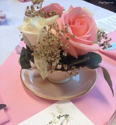 pink roses in a teacup on a table at a formal dinner party with menus and utensils