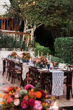 an outdoor dining table set with flowers and candles