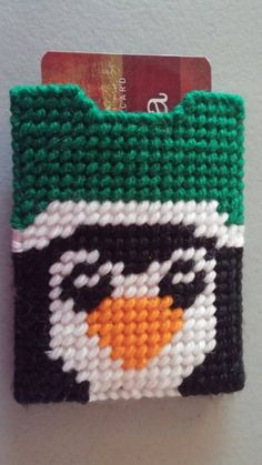 a green and white knitted card holder with a penguin on it's face