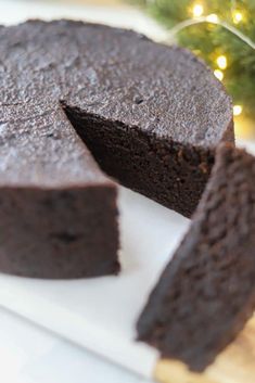 a chocolate cake is cut into pieces on a cutting board with a christmas tree in the background