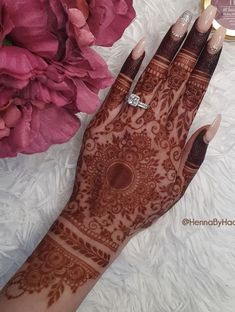 a woman's hand with henna on it and pink flowers in the background