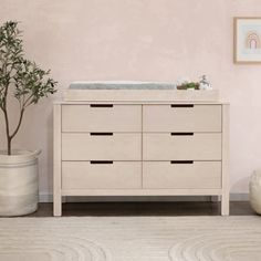 a white dresser with drawers and a baby crib in the corner next to a potted plant