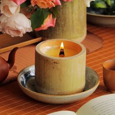 a lit candle sitting on top of a plate next to a tea pot and cup