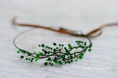 a headband with green beads on it sitting on top of a white table next to a brown ribbon