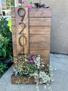 a wooden sign sitting next to flowers on top of a planter in front of a building