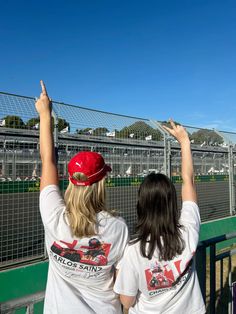 two women standing next to each other in front of a fence