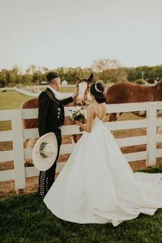 a bride and groom standing in front of a white fence next to a brown horse