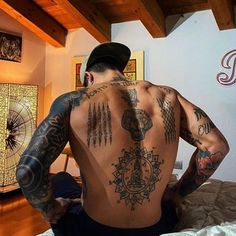 a man with tattoos on his back sitting on a bed