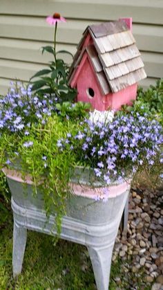 an old tub is filled with purple flowers and a birdhouse in the back yard