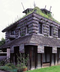 an old wooden building with plants growing on the roof and grass growing on it's roof