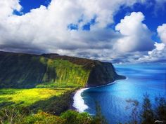 the ocean is blue with white clouds and green grass on the cliffs, as well as an island in the distance