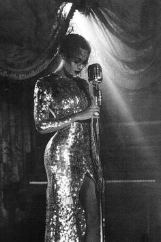 a woman in a sequin dress holding a microphone and standing next to a curtain