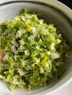 a white bowl filled with lettuce next to a wooden spoon