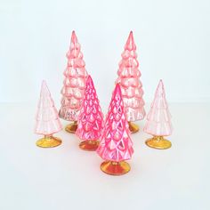 pink glass christmas trees are lined up on gold bases and stand against a white background