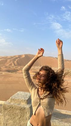 a woman standing in the desert with her arms up